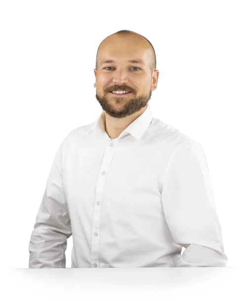 Michael Binder steht mit weißem Hemd hinter einem Tisch und blickt lächelnd in die Kamera.