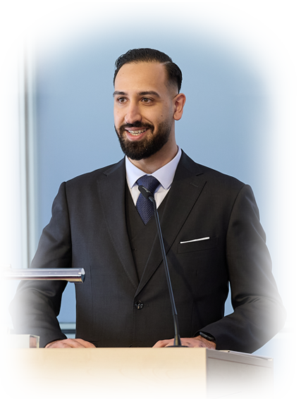 Navid Sheikh steht im Anzug am Rednerpult