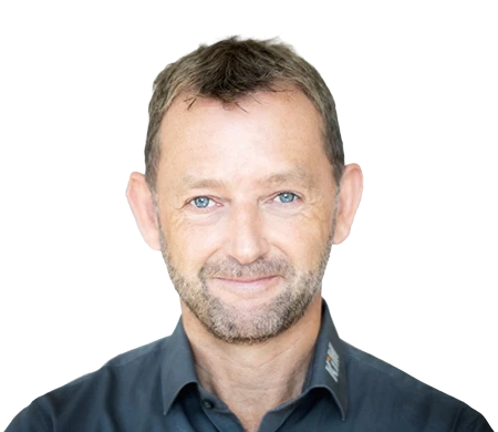 Achim Angel, Geschäftsführer der KiM GmbH – Member of 4PACE, lächelt freundlich in die Kamera. Er hat kurzes, braunes Haar, einen kurzen Bart und trägt ein dunkelgraues Hemd mit leicht geöffnetem Kragen. Im Hintergrund ist eine geschwungene Wellenform in Weiß, Hellblau und Dunkelblau zu sehen, die dem Bild eine moderne Gestaltung verleiht.