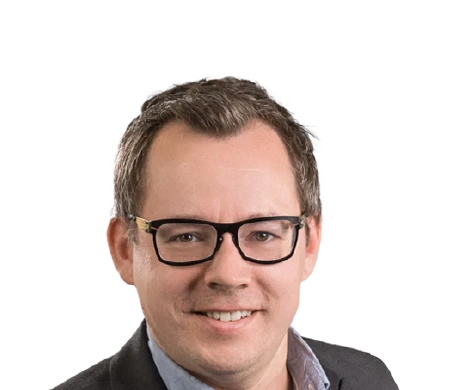 Dominik Fimberger, Head of Marketing and E-Commerce at Weyland Steiner, smiles at the camera. He is wearing dark-rimmed glasses, a light blue shirt with an open collar and a gray jacket over it. His hair is short and brown and he has no beard.