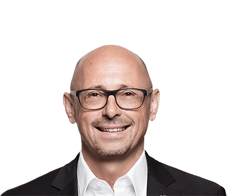 Günther Rossdeutscher, associé gérant d'asecos, regarde aimablement la caméra. Il porte des lunettes noires, une chemise blanche et une veste sombre. Il est chauve avec une courte barbe.